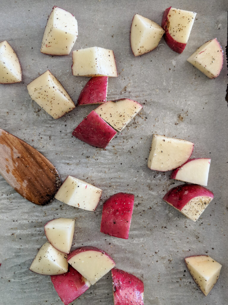 Quartered red potatoes are tossed on a parchment paper lined baking sheet with olive oil and salt and pepper before going into the oven.