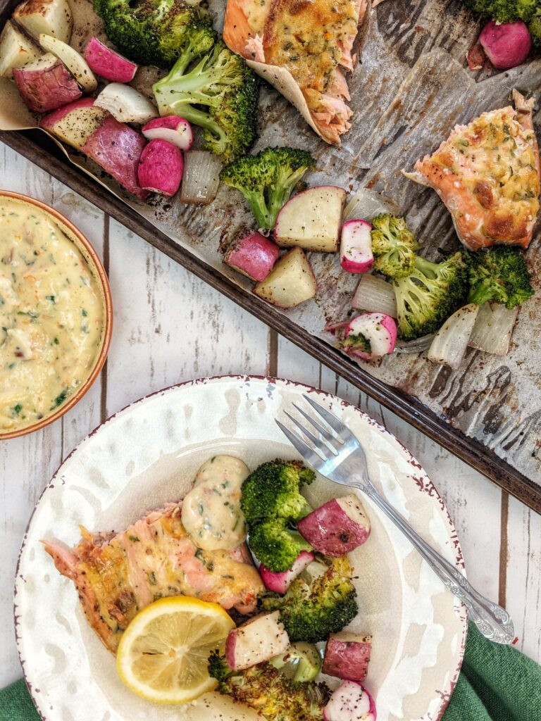 Whole30 compliant salmon fillet and roasted vegetables are served straight from a baking sheet alongside a homemade sun-dried tomato aioli and a squeeze of fresh lemon juice.