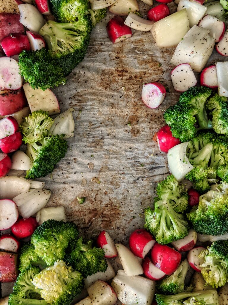 Roasted red potatoes are tossed on a baking sheet with radishes, broccoli and onions and then pushed towards the outskirts of the baking sheet to make room for the salmon fillet.