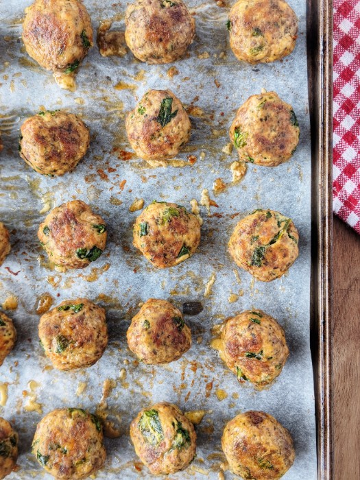 Baked Italian Meatballs are evenly distributed on a parchment paper-lined baking sheet fresh out of the oven. 