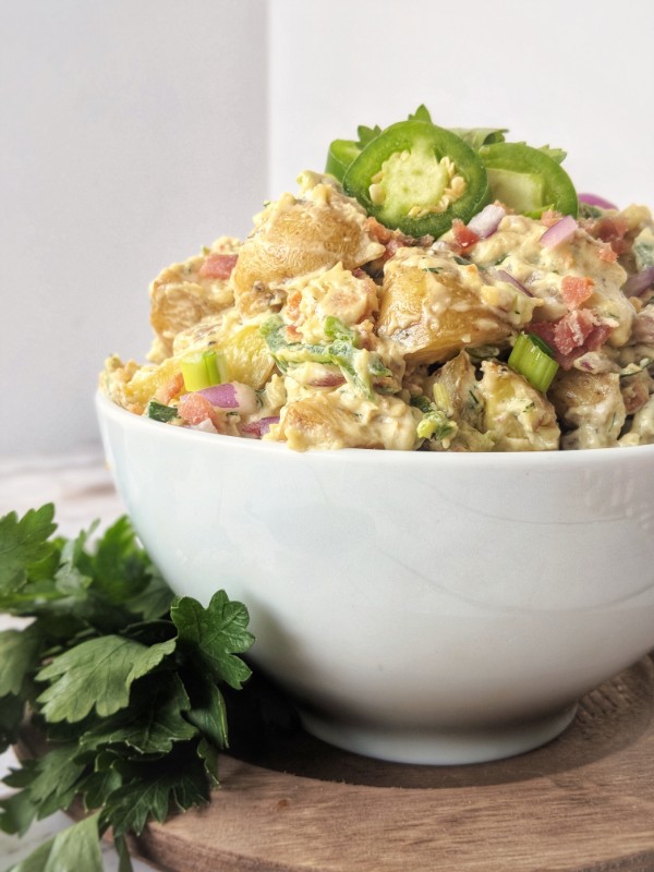 Creamy Dairy-Free Loaded Baked Potato Salad is piled high in a white bowl, garnished with a sprig of parsley and fresh jalapeno slices.