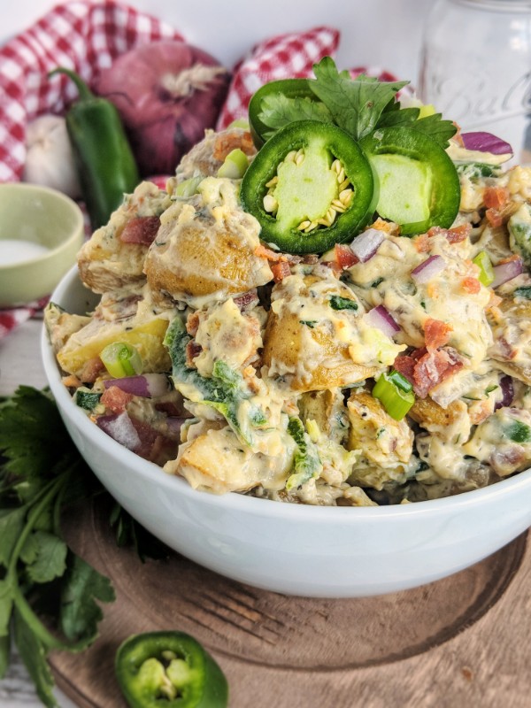 Whole30 Loaded Baked Potato Salad is piled high in white bowl and garnished with red onion, green onion, jalapenos and fresh flat-leaf parsley.