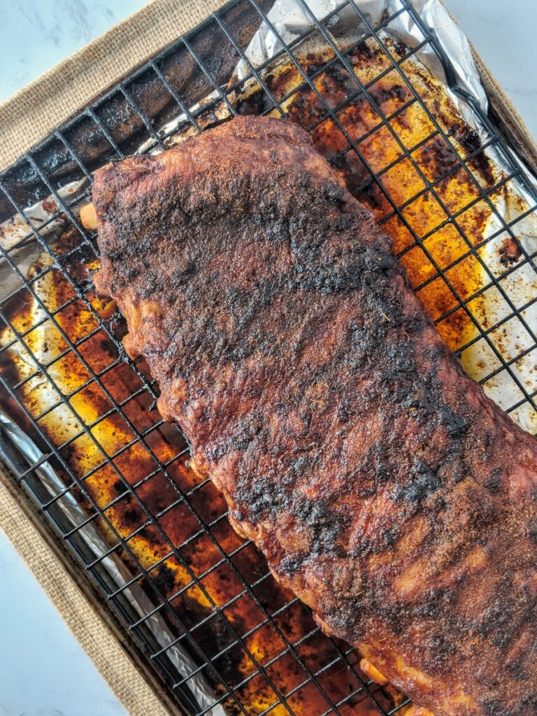Baked Memphis-style ribs fresh from the oven are resting above a wire rack positioned above a foil-lined baking sheet ready to be sliced.