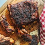 Baked Memphis-style moist and juicy dry rubbed ribs are sliced on a wooden cutting board.
