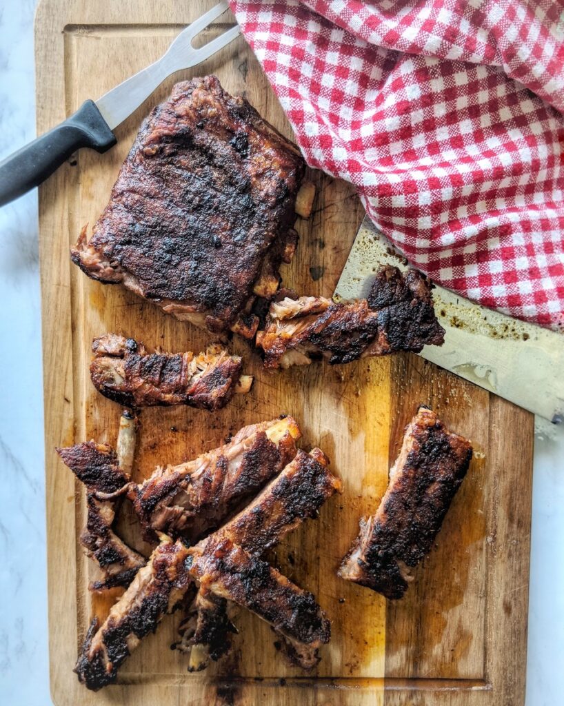 After resting for 5 to 10 minutes, freshly baked Keto, Paleo & Whole30 pork ribs are sliced and served on a wooden cutting board. 