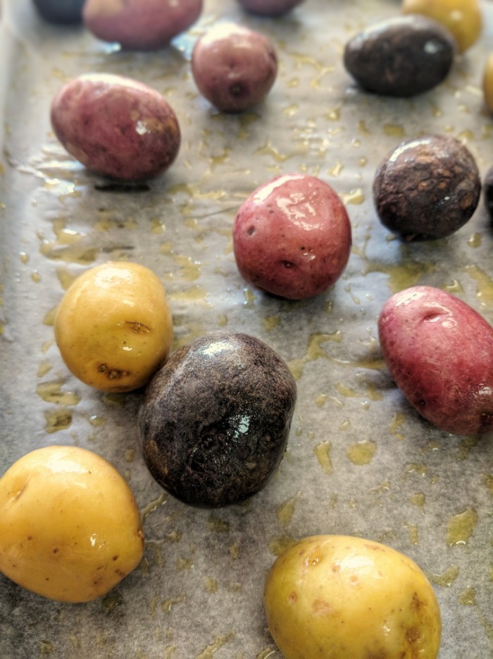 Whole30 compliant medley of small potatoes are tossed in extra virgin olive oil on a piece of parchment paper. 