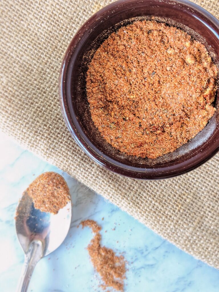 A blend of sugar-free and Whole30 compliant BBQ spices fills a small brown ramekin positioned above a burlap tablecloth.