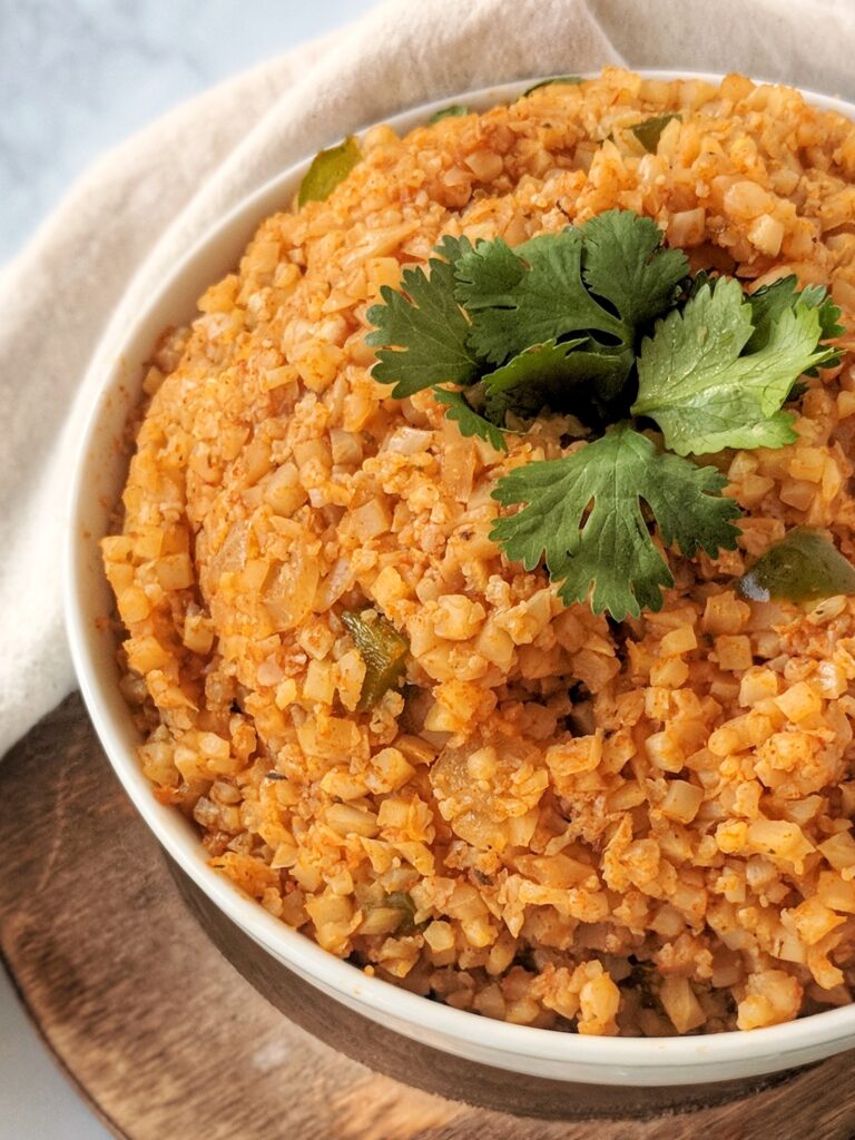 Low carb & Keto-friendly vibrant orange Spanish Cauliflower Rice is served in a large white bowl and garnished with fresh chopped cilantro.