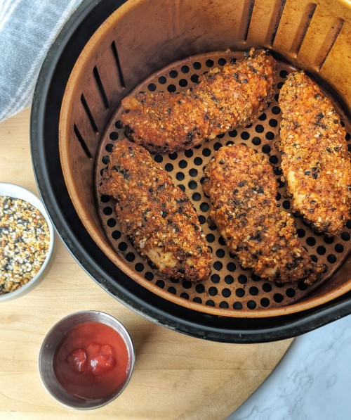 Whole30 compliant chicken tenders are presented in a copper air fryer basket, alongside a bowl of everything bagel seasoning and ketchup.