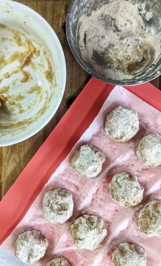 A grain-free Orange Chicken Meatball mixture is rolled into bite-size balls, dredged through a cassava flour based breading and set aside on a piece of parchment paper ready to be cooked.