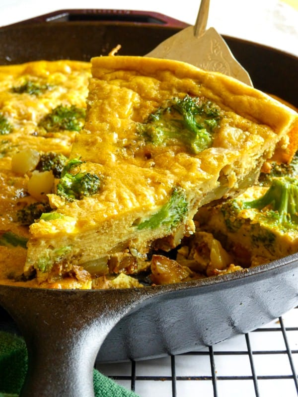 A slice of freshly baked dairy-free Smoked Sausage and Potato Frittata with Broccoli is served straight from a cast iron skillet.