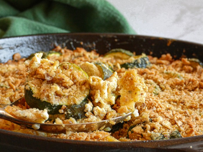 A generous helping of Whole30 Zucchini au Gratin is spooned from a heavy oven-safe-skillet. 