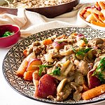 Plated in a shallow bowl is a generous serving of rich, creamy and delicious Paleo Beef Stroganoff served over buttery potatoes and carrots and garnished with fresh dill. A skillet of stroganoff and a plate of potatoes and carrots is also on the table.