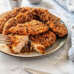 Crisp and juicy air fried chicken tenders are crisped to perfection and served on a platter. One chicken strip is cut into showing the perfectly cooked inside.