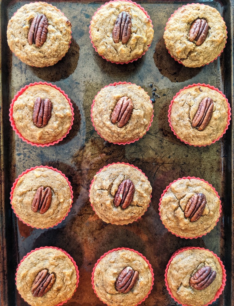 Freshly baked grain-free Maple Pecan Banana Bread Muffins in red silicone baking cups are placed on a baking sheet.