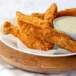 Keto, Paleo & Whole30 Air Fryer Fried Pickles are stacked on a small plate and served beside a small bowl of ranch dressing.