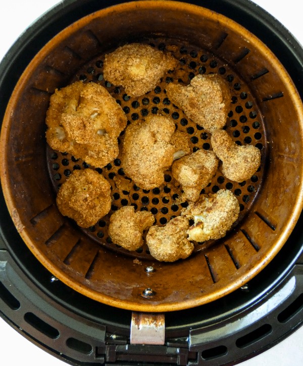 Grain-free almond flour breaded cauliflower florets are cooked in a single-layer in an air fryer oven. 